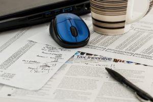 Laptop, Coffee Mug, And Pen On Top Of Financial Paperwork + Thinking Ahead on Income Taxes