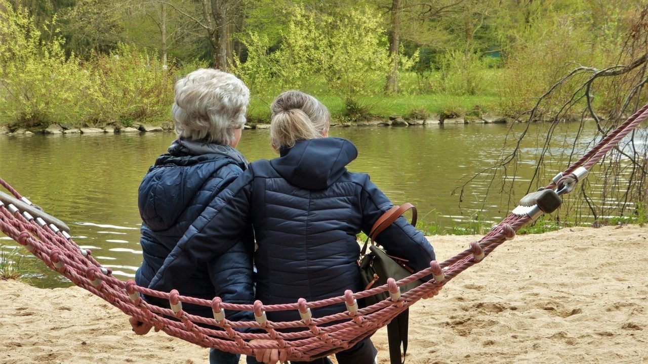 A Women Sitting On A Hammock With Her Mother By The River